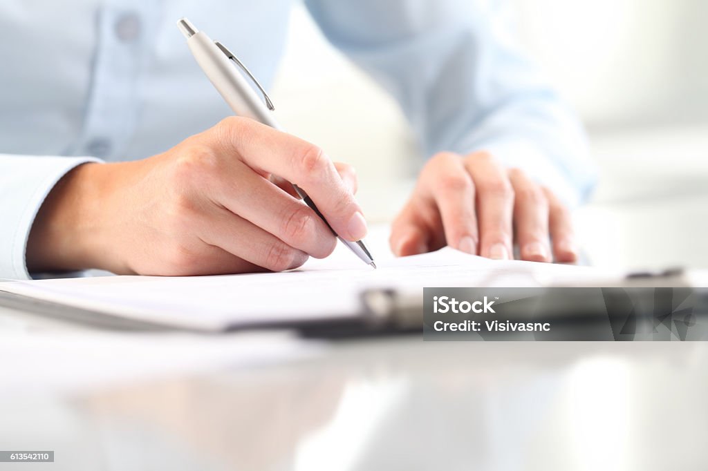 Woman's hands writing on sheet in clipboard with a pen Woman's hands writing on sheet in a clipboard with a pen; isolated on desk Form Filling Stock Photo