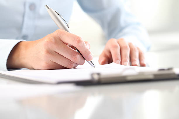 Woman's hands writing on sheet in clipboard with a pen Woman's hands writing on sheet in a clipboard with a pen; isolated on desk filling out stock pictures, royalty-free photos & images