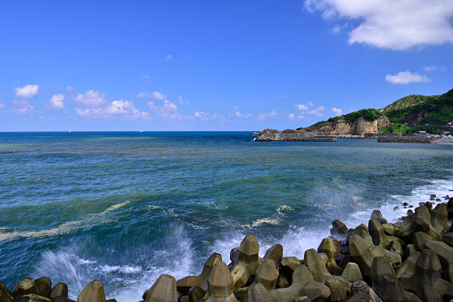 Beautiful seashore with sea waving at the pacific ocean. Blue ocean,wet wave breaker blocks and white spoondrift. White clouds floating at blue sky,sunlight and sunny weather. Northeast coast national scenic area,Taiwan.