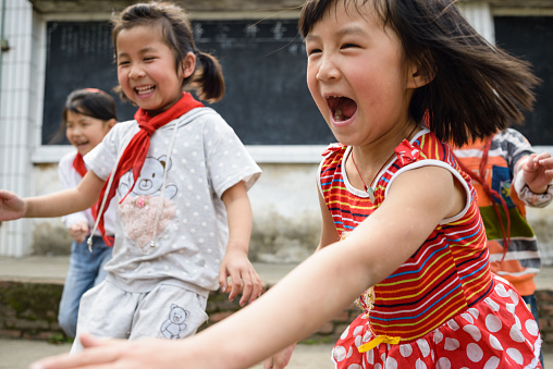 A group of four joyous 6-8 year old elementary age Chinese school kids running in the school yard, laughing and shouting, having a great time.