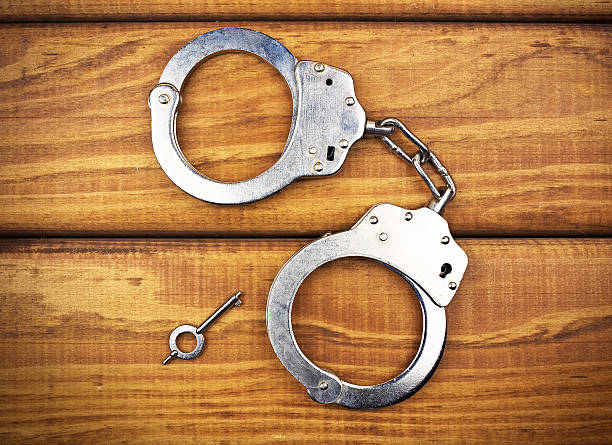 istock Steel metallic handcuffs on a wooden table 613542434