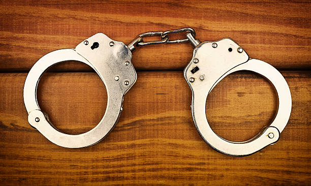 istock Steel metallic handcuffs on a wooden table 613542676
