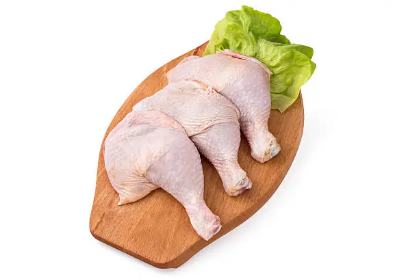 Fresh raw chicken legs arrangement on kitchen cutting board with lettuce