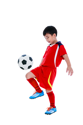 Full length portrait of happy asian soccer player in red uniform bounce his soccer ball, studio shot. Isolated on white background.
