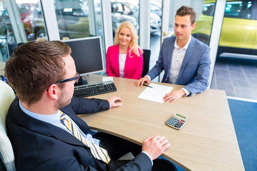 Couple buying car at dealership and negotiating price with salesman