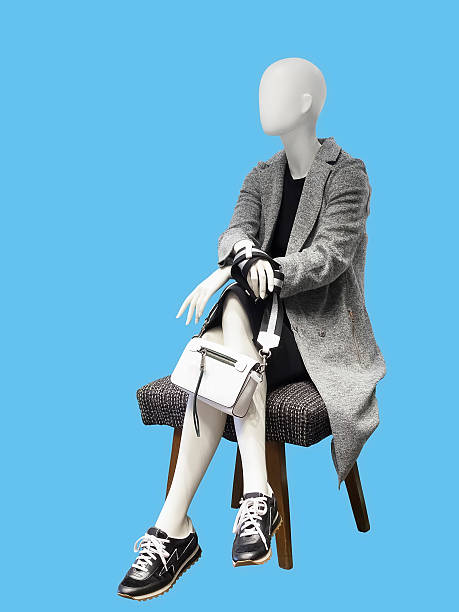 Sitting female mannequin wearing gray coat, isolated on blue background. No brand names or copyright objects.