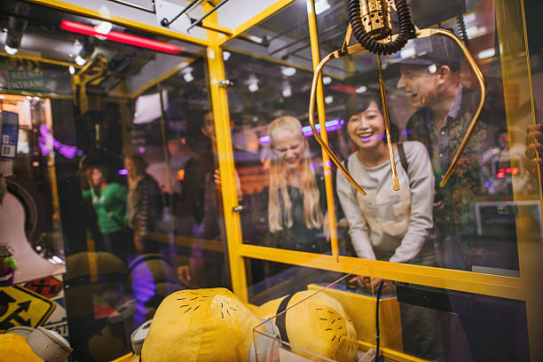 Woman playing toy grabbing game with friends Happy young woman playing toy grabbing game with friends at amusement park. arcade photos stock pictures, royalty-free photos & images