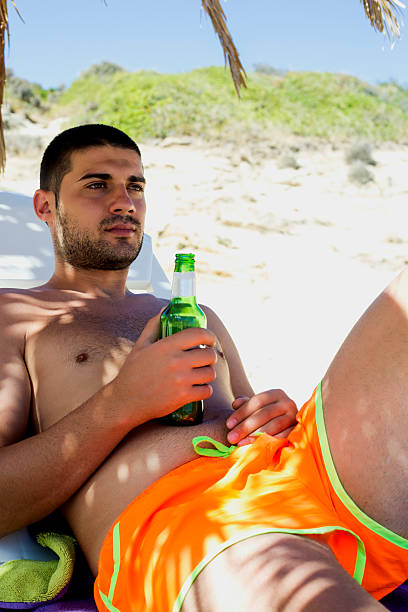 istock Young man drinking beer on the beach 613561988