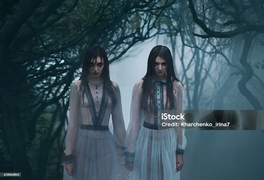 Creepy lady with long black hair looking at you The girls are crying. Young ladies in ancient dresses walking through the woods in search of a victim. Foggy, spooky forest. Photoshoot in the style of horror. Mystical photo. Fashionable tinted.Creative color. Forest Stock Photo