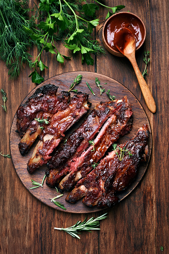 Grilled sliced barbecue pork ribs, green herbs and tomato sauce, top view