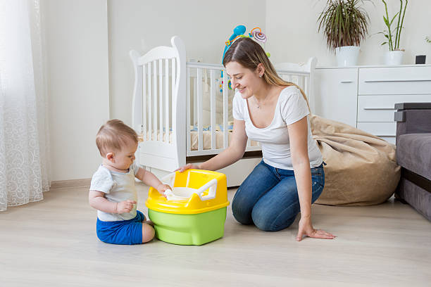 Young mother teaching her baby how to use chamber pot Young smiling mother sitting on floor at living room and teaching her 10 months old baby boy how to use chamber pot potty toilet child bathroom stock pictures, royalty-free photos & images