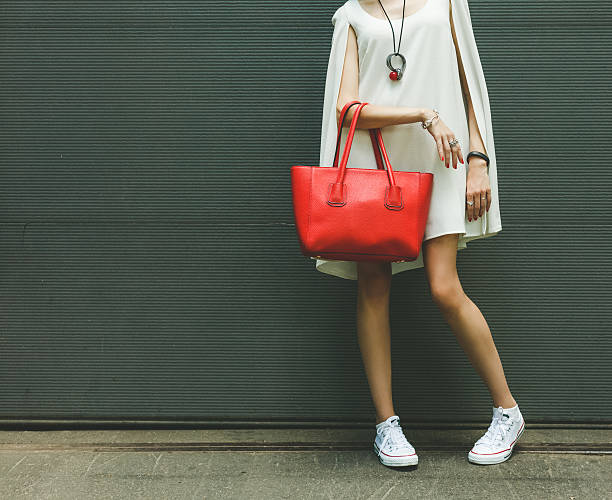 Fashionable big red handbag on the arm of the girl Fashionable beautiful big red handbag on the arm of the girl in a fashionable white dress and sneakers, posing near the wall on a warm summer night. Warm color. purse photos stock pictures, royalty-free photos & images