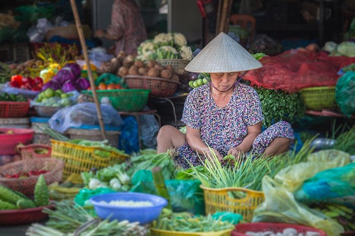 Hue, Vietnam - November 17, 2015: Old woman selling vegetables in the hue market.  Hue is the former capital of Vietnam - her traditional hat is seen all over Vietnam 
