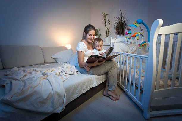 istock Adorable baby sitting on mothers lap and reading book 613657000