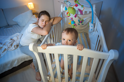 Young tired mother got asleep next to baby's crib