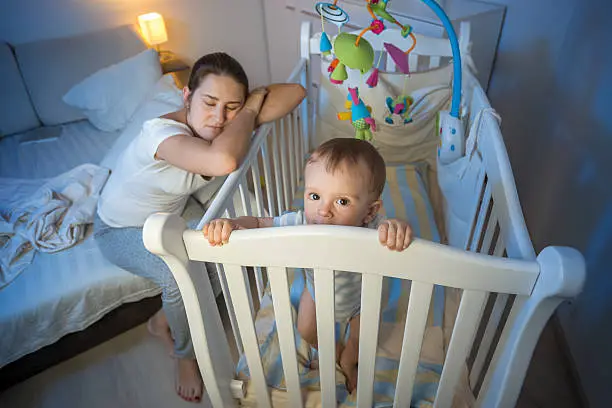 Young tired mother got asleep next to baby's crib