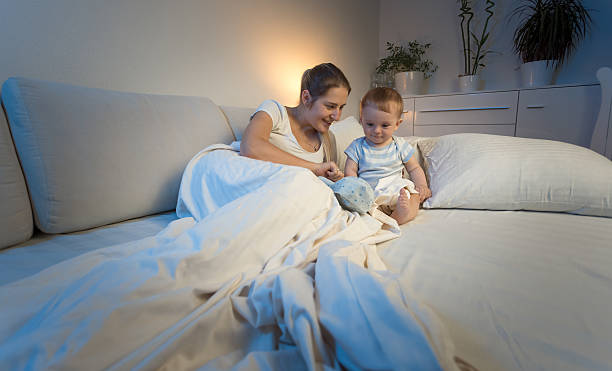 istock Mother playing with baby on bed at night 613658230