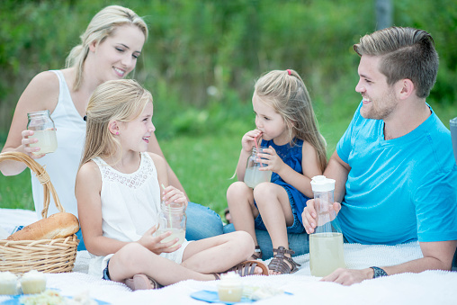 A young family is having a picnic together at the park on a warm sunny day. They are drinking lemonade.