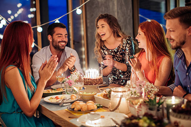 Applause for the bithday girl! Friends having dinner party at home. Celebrating birthday party for their friend. They are happy and well dressed. Home is decorated with festive string lights and candles. Evening or night. woman birthday cake stock pictures, royalty-free photos & images