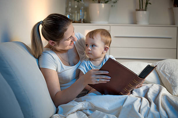 istock Mother in bed with baby at night holding book 613659740