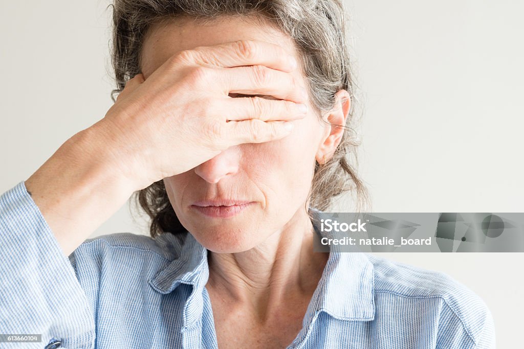 Middle aged woman with hand over eyes Close up of middle aged woman with hand covering eyes Menopause Stock Photo