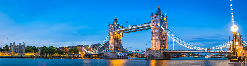 Panoramic view across the River Thames to the historic span of Tower Bridge illuminated against the blue dusk sky overlooked by the glittering lights of the Embankment in the heart of London, Britain's vibrant capital city