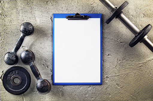 Fitness or bodybuilding concept background. Product photograph of old iron dumbbells on grey, conrete floor in the gym with blank page. Photograph taken from above, top view with lots of copy space