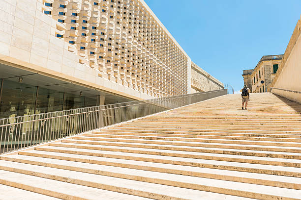 New modern architecture, the Parliament, and broad new monumental stairways leading up to the ancient fortifications of city of Valletta,  a Unesco World Heritage City. One man with backpack walking up the stairways on sunny summerday.