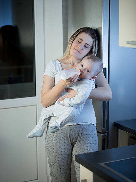 istock Sleepy mother feeding baby from bottle on kitchen at night 613663200