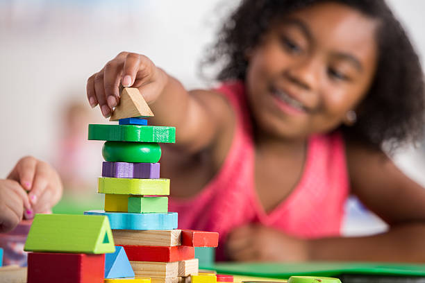 Pretty African American little girl smiles while creating something with wooden blocks at daycare. Focus is on the wooden blocks.