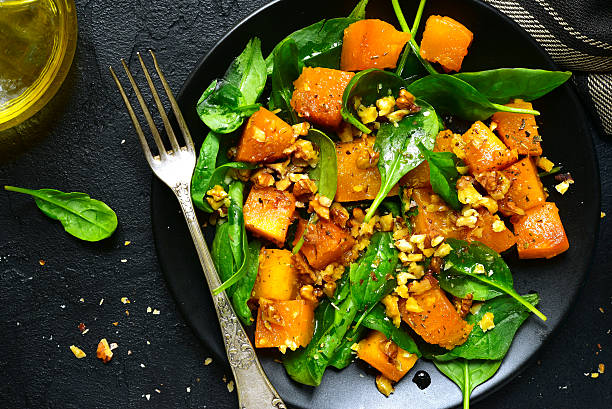 Roasted pumpkin salad with spinach and walnut .Top view. Roasted pumpkin salad with spinach and walnut on a black plate on a stone background.Top view. squash vegetable stock pictures, royalty-free photos & images