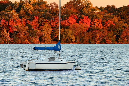 A sail boat is moored at the marina on Lake Harriet against a colorful autumn background in Minneapolis, Minnesota.