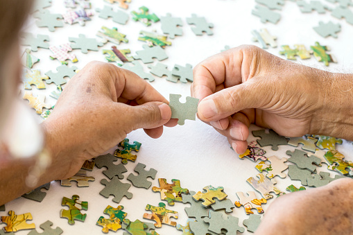 Senior couple is playing puzzle on white table.