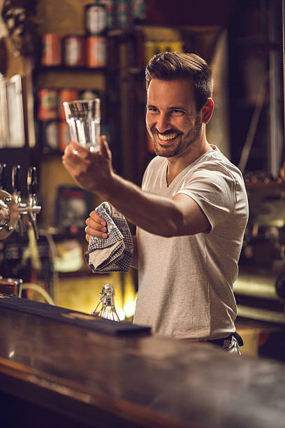 istock Happy bartender cleaning drinking glass at bar counter. 613689256