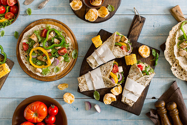 Roll tortilla with grilled chicken fillet on wooden cutting boar Roll tortilla with grilled chicken fillet on a wooden cutting board on blue wooden table with grilled vegetables, Top view. Outdoors Food Concept mexican culture food mexican cuisine fajita stock pictures, royalty-free photos & images