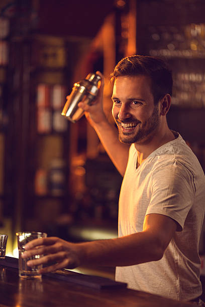Young smiling male barista preparing cocktail at bar counter.