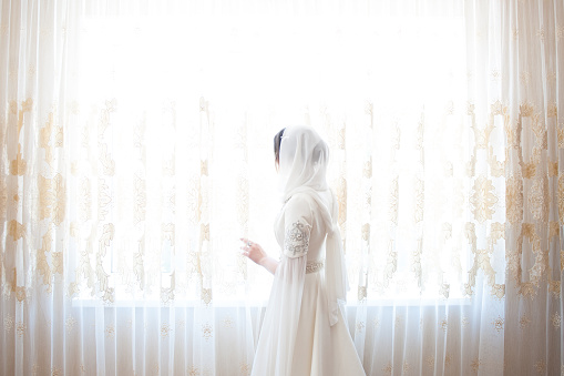 muslim woman in a white headscarf looking out the window