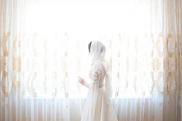 muslim woman in a white headscarf looking out the window