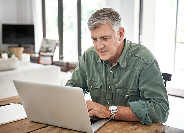 Getting to grips with the world online Cropped shot of a mature man working on his laptop at home mature men stock pictures, royalty-free photos & images