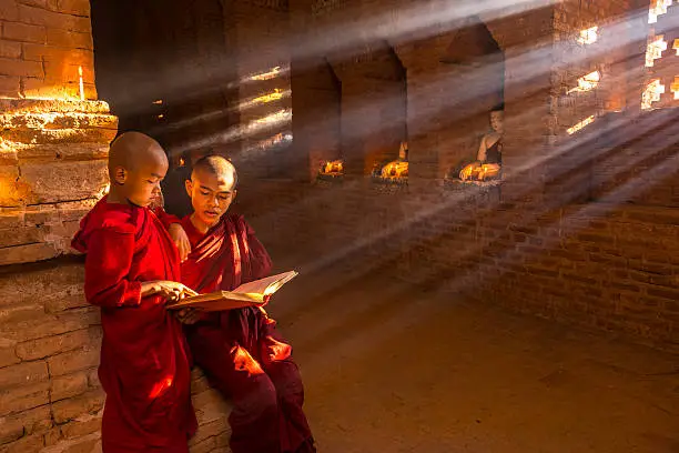 Two young buddhist monks praying inside the temple in Bagan, Myanmar