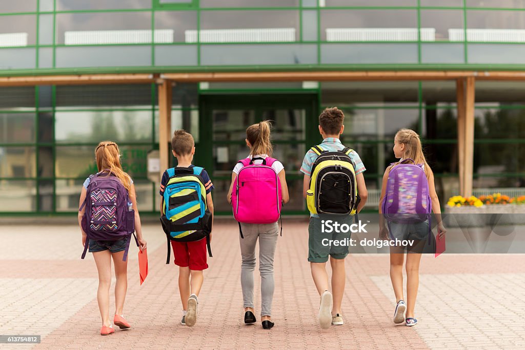 group of happy elementary school students walking primary education, friendship, childhood and people concept - group of happy elementary school students with backpacks walking outdoors from back Backpack Stock Photo