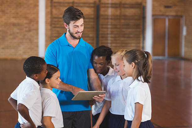 Sports teacher and kids using digital tablet in basketball court Sports teacher and school kids using digital tablet in basketball court at school gym physical education stock pictures, royalty-free photos & images