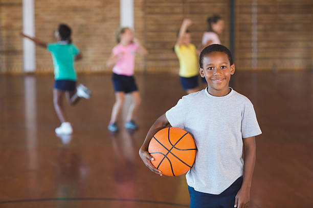 Boy standing with ball in basketball court Boy standing with ball in basketball court at school gym youth basketball indoor stock pictures, royalty-free photos & images