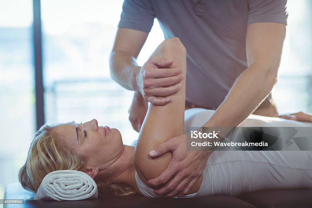Donna che riceve la terapia della spalla dal fisioterapista - Foto stock royalty-free di Fare lo stretching