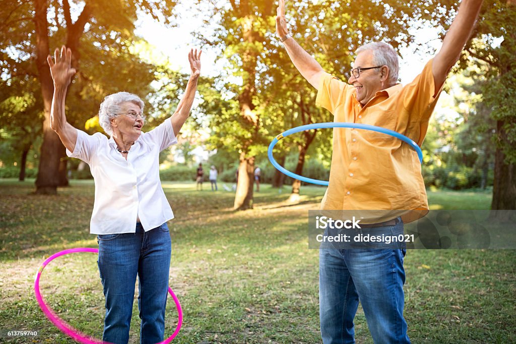 Feliz pareja de ancianos divertido jugando hulahop en el parque - Foto de stock de Tercera edad libre de derechos