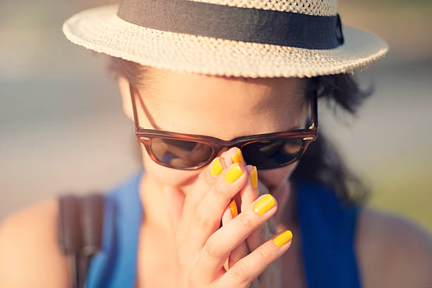 girl covering her nose and mouth with her hands girl with straw hat and sunglasses covering her nose and mouth with her hands yellow nail polish stock pictures, royalty-free photos & images