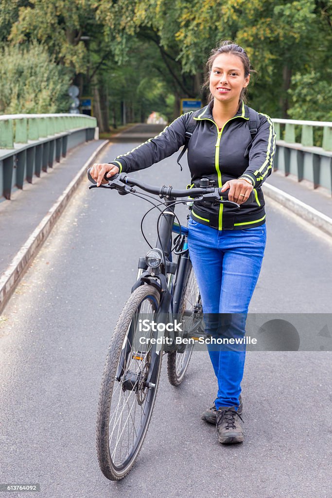 Dutch woman standing with ATB mountainbike on bridge European woman standing with ATB mountainbike on bridge. The dutch woman is very sportive or sporty. She is posing for the camera on a metal bridge in the netherlands. In my country a lot of people do some kind of sport in their leisure time. It's healthy to move your body and get active. Concept of activity, bicycle, bike, biking, traffic, transport, female, feminine. Activity Stock Photo