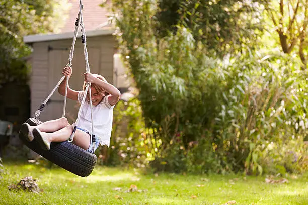 Young Girl Playing On Tire Swing In Garden