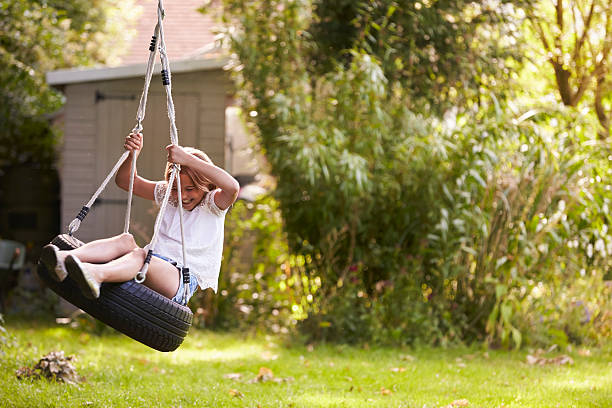 молодая девушка играет на шины качели в саду - tire swing стоковые фото и изображения