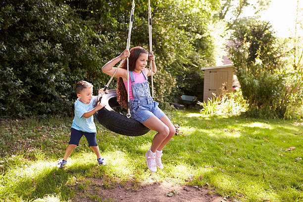 brother pushing sister on tire swing in garden - tire swing imagens e fotografias de stock